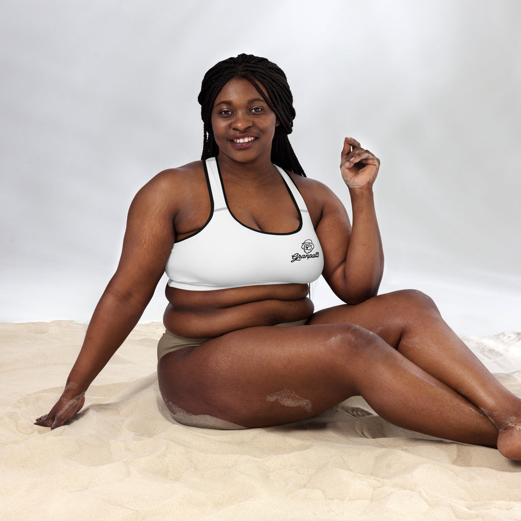 Woman wearing a white sports bra and beige shorts sitting on sand with a white background