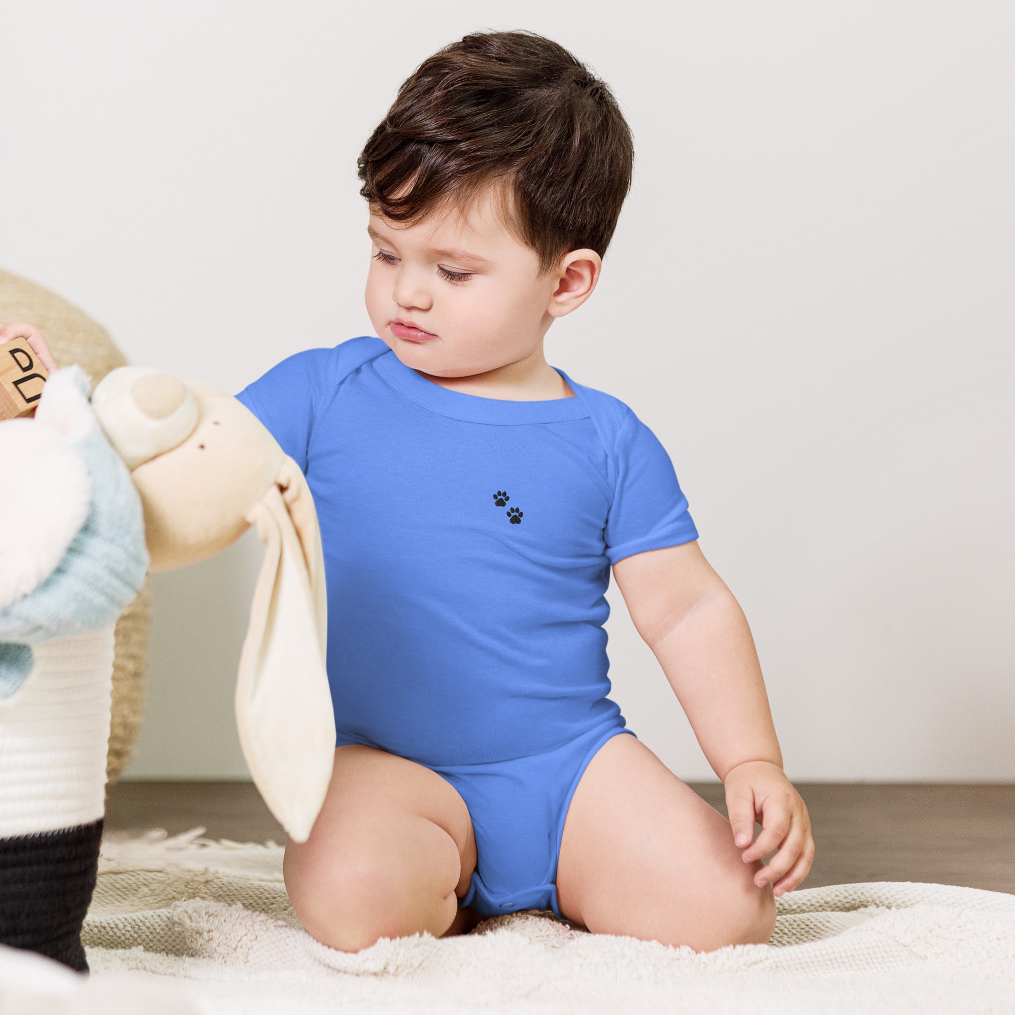 Child wearing a blue onesie with paw prints, sitting on a carpeted floor.