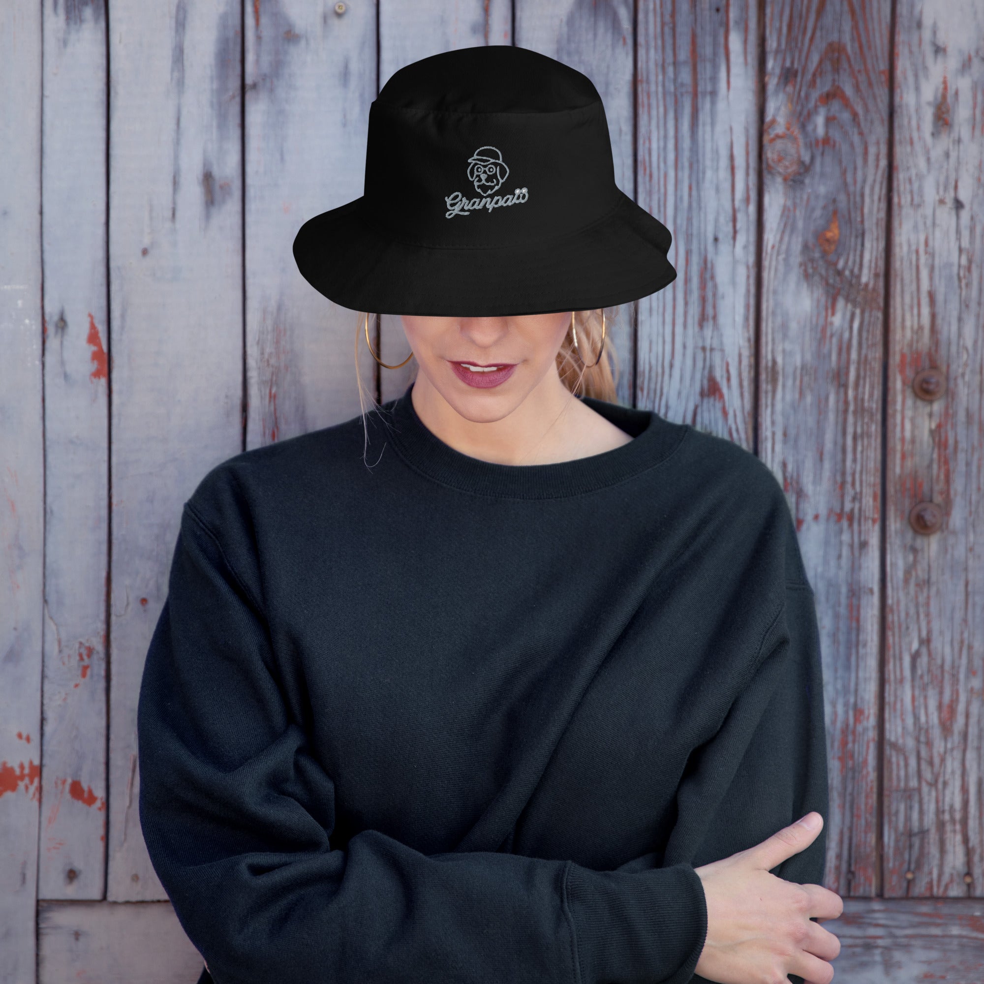 Person wearing a black bucket hat and sweatshirt against a wooden background