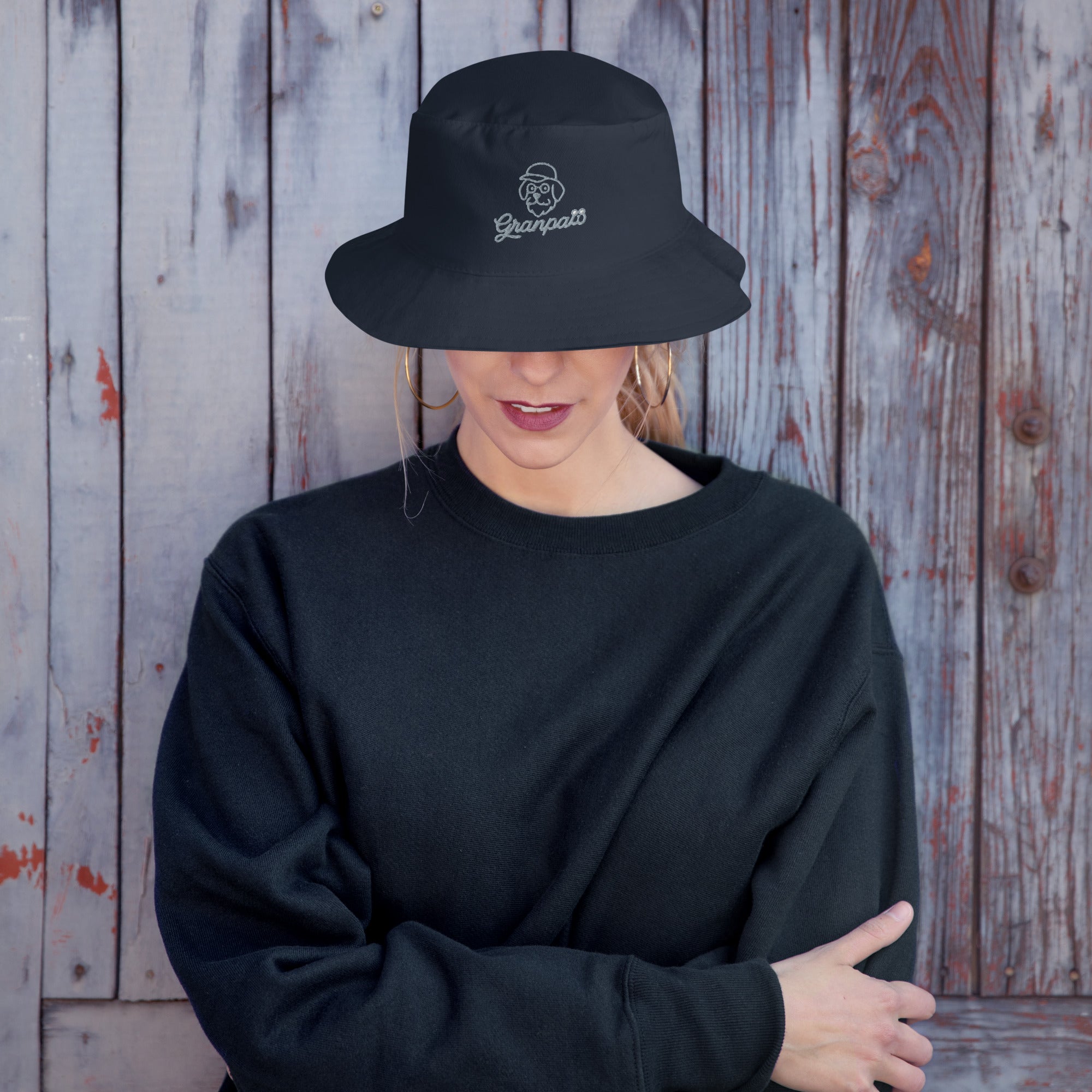 Person wearing a black bucket hat and sweatshirt against a wooden background