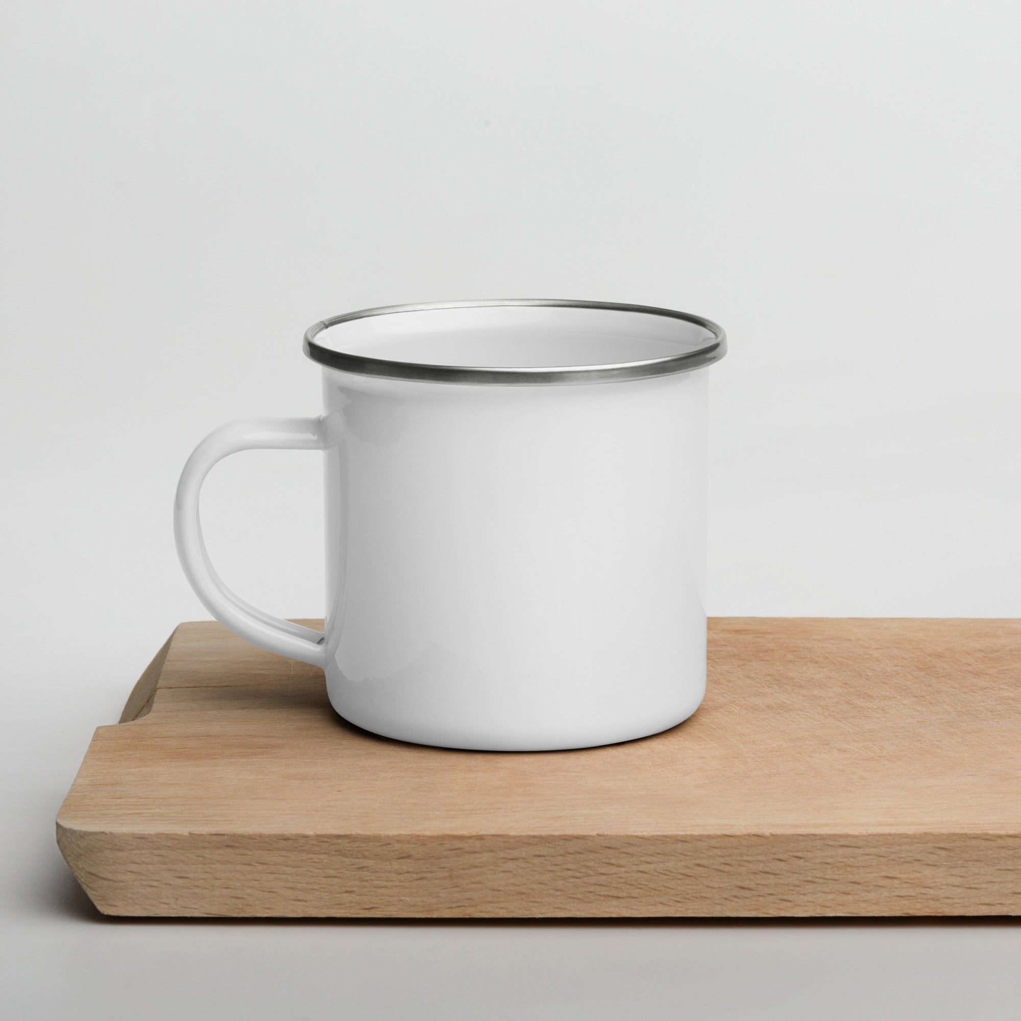 White enamel mug with black rim on a wooden surface against a light gray background