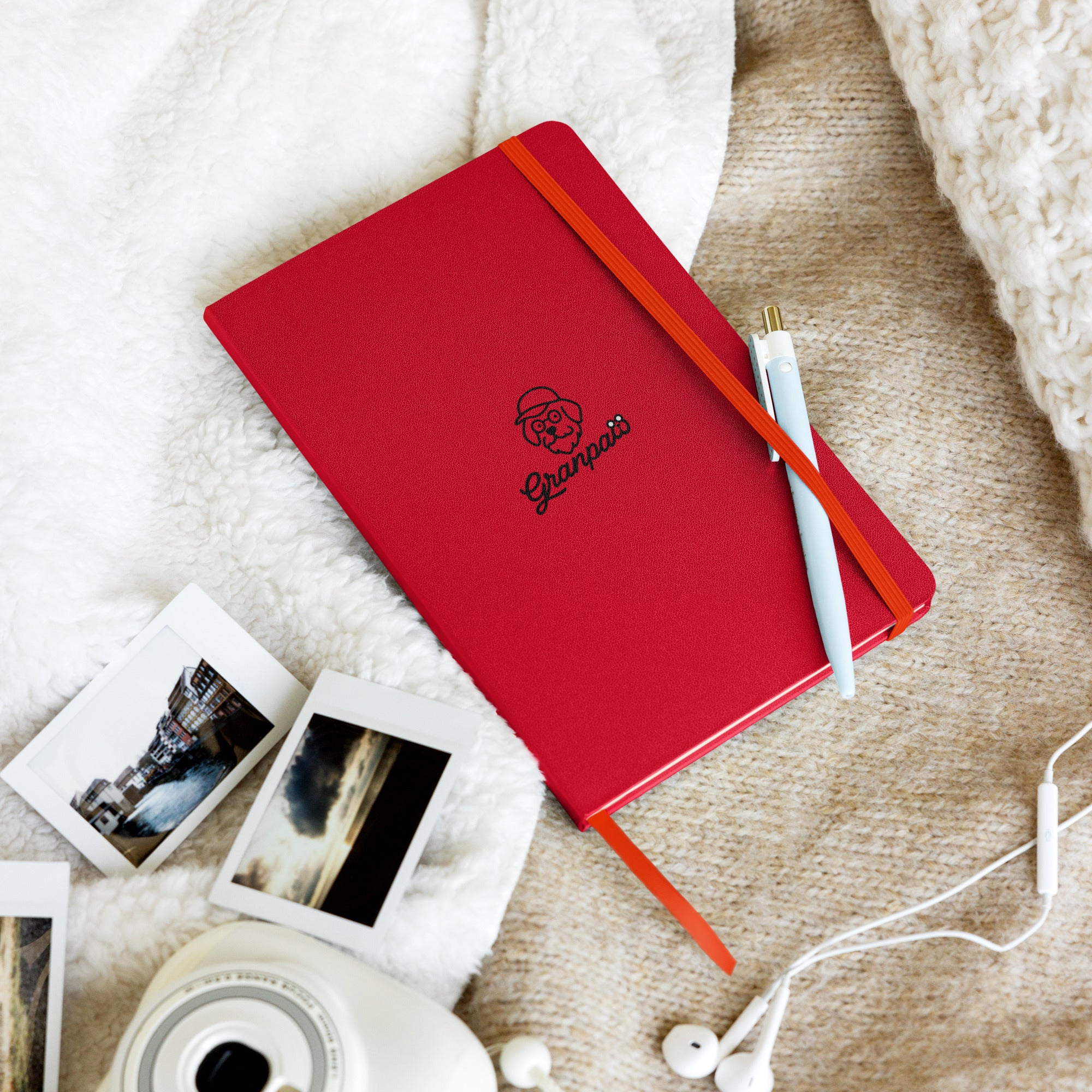 Red notebook with a logo, white camera, and earphones on a textured surface