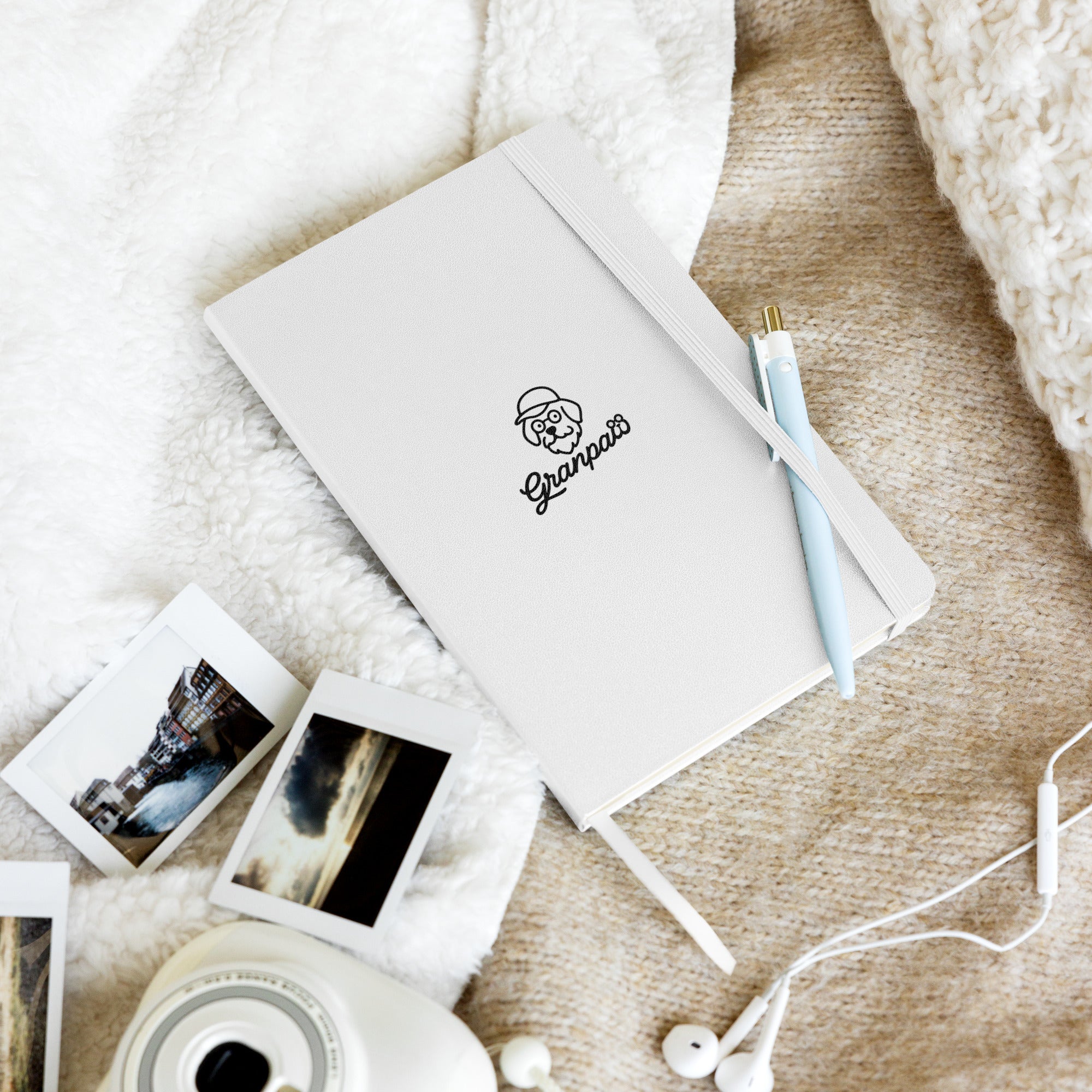 White notebook with a logo, instant photos, and earphones on a textured surface