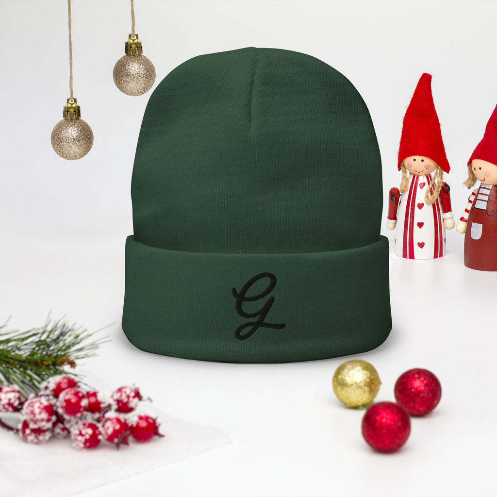 Green beanie with a monogram 'G' on a white background with Christmas decorations.