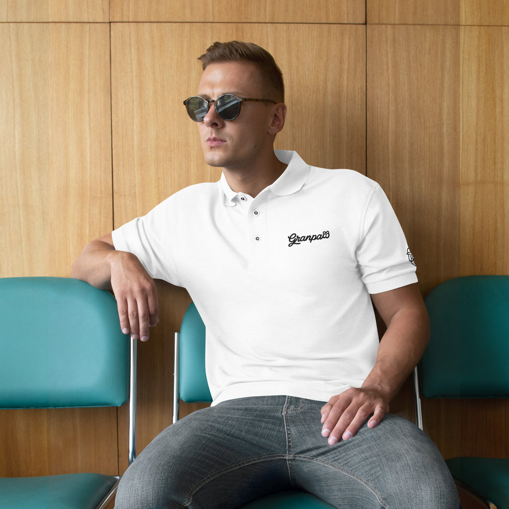 Man wearing a white polo shirt with a brand logo, sitting against a wooden wall.