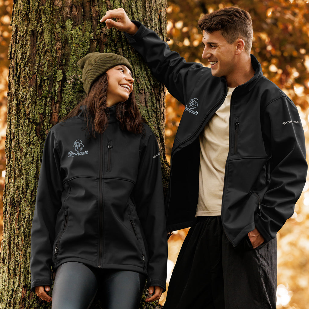 Two people wearing Columbia jackets standing next to a tree in an autumn setting.