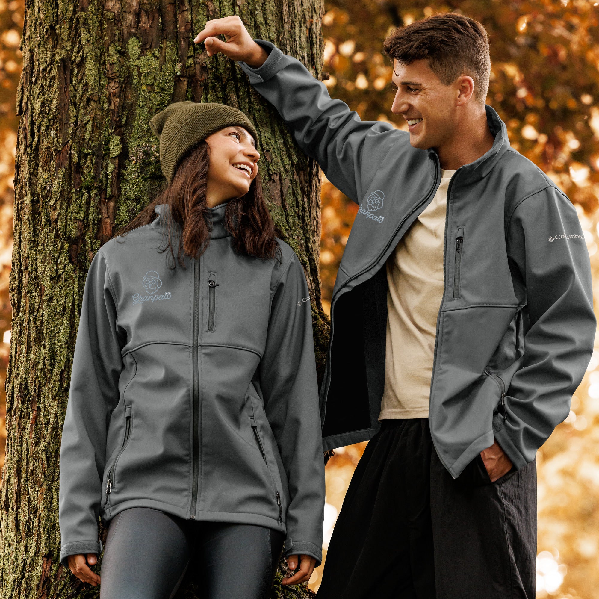 Two people wearing gray jackets standing next to a tree in an autumn setting