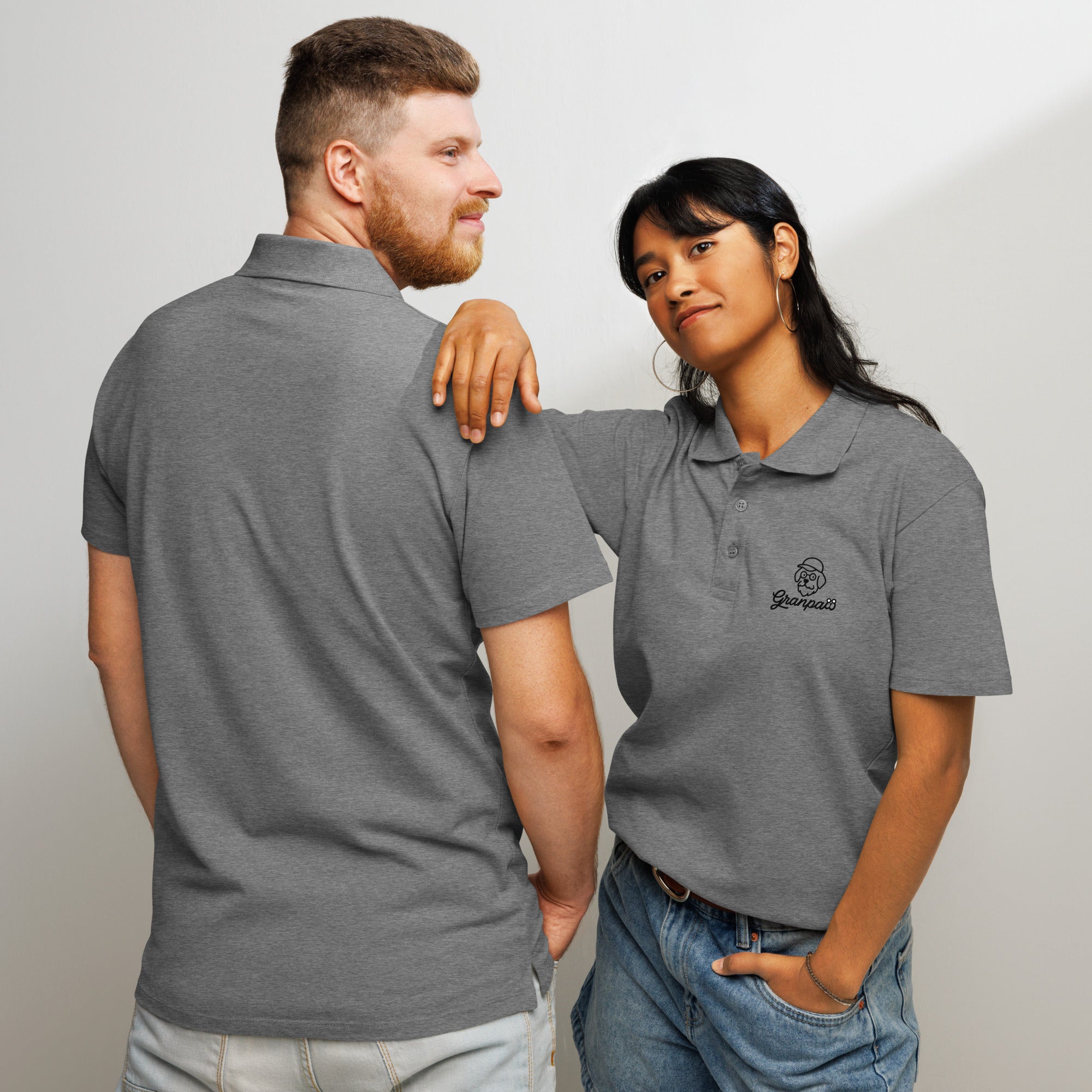 Two people wearing gray polos with a brand logo, standing close together against a plain background.