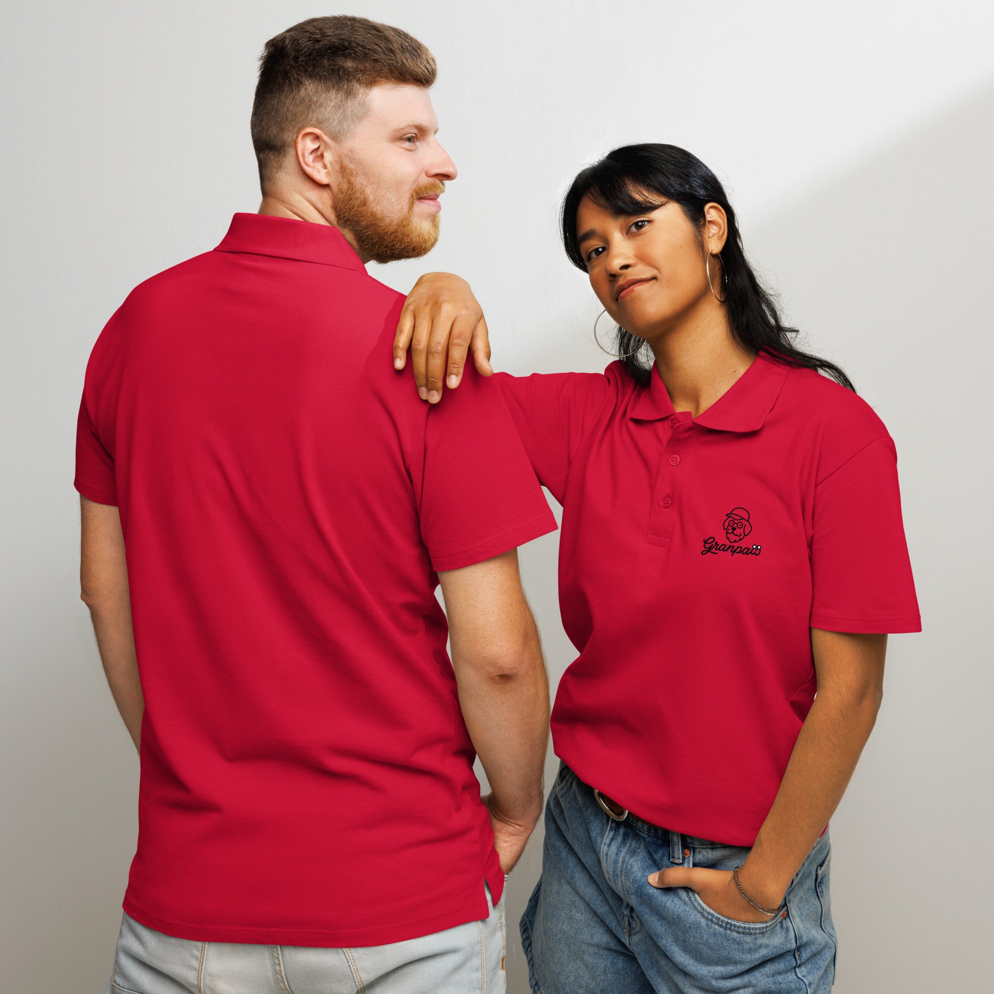 Two people wearing red polo shirts with a logo on a plain background