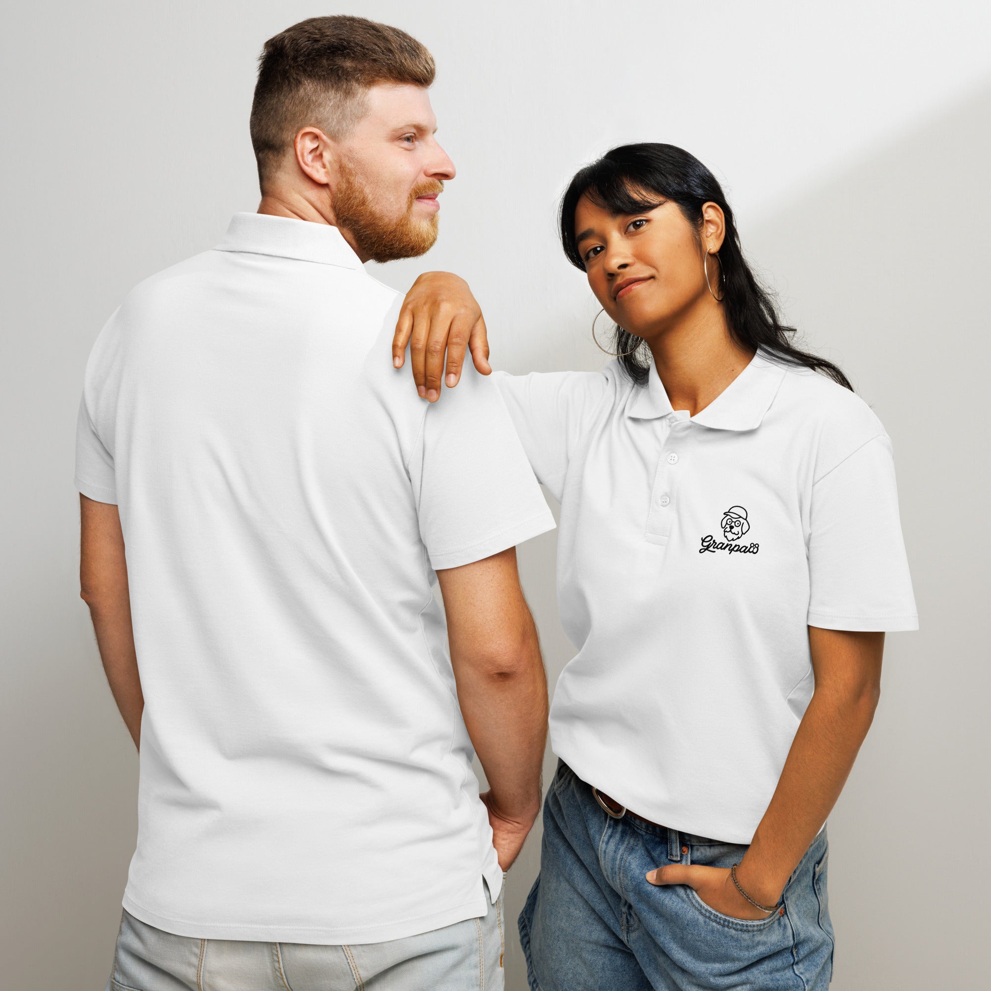 Two people wearing white polos with a logo, standing close together against a plain background.