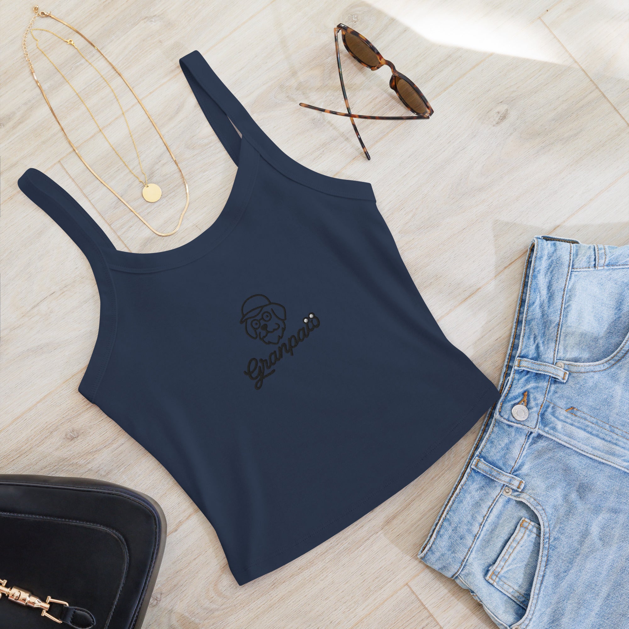 Navy blue tank top with a logo, sunglasses, necklace, and jeans on a light wooden surface