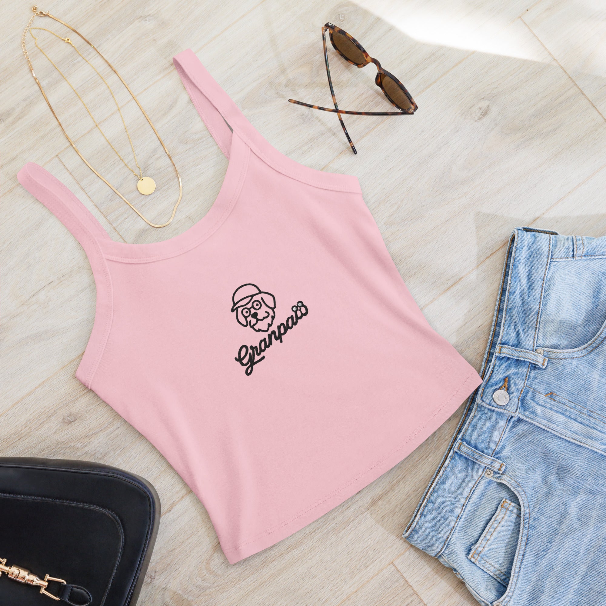 Pink tank top with 'Ganapati' logo, sunglasses, necklace, and jeans on a light wooden surface