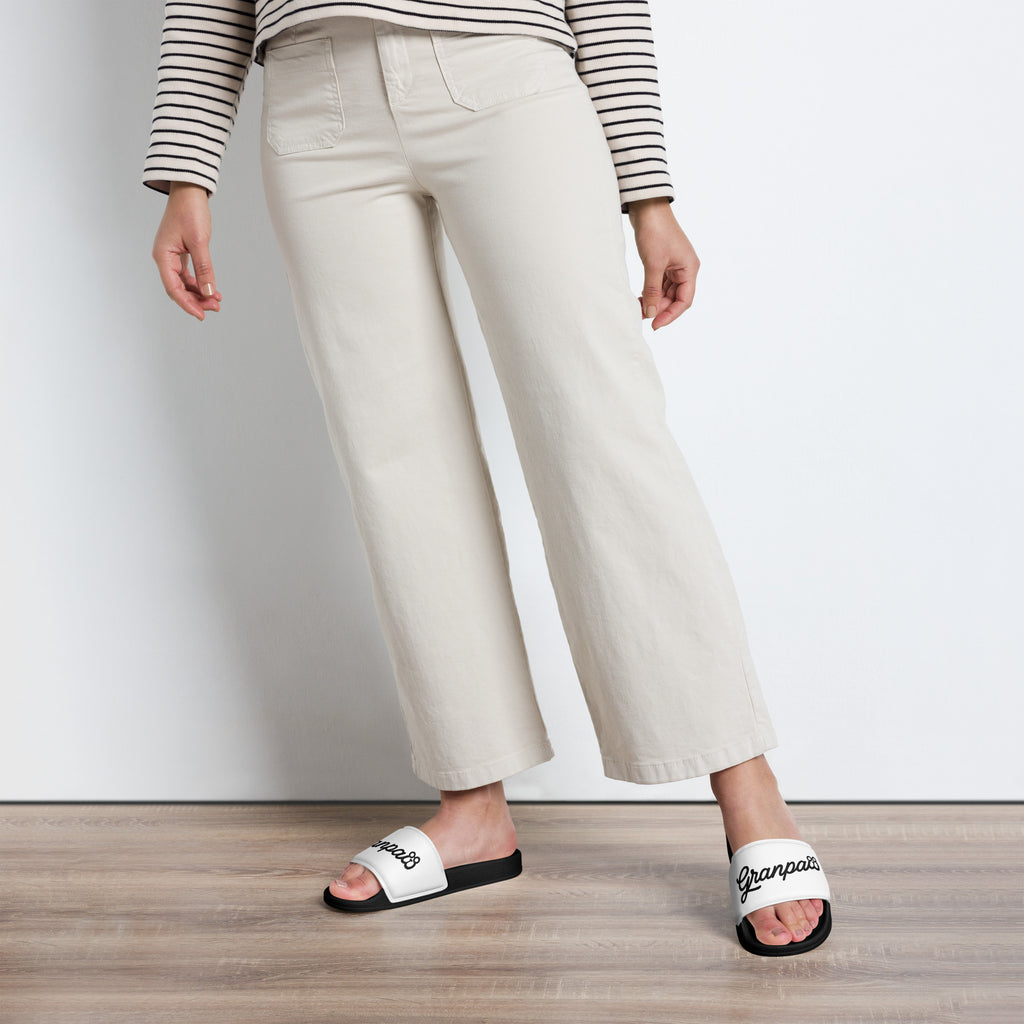 Person wearing white wide-leg pants and white slides with 'granpaw golf' branding on a wooden floor.