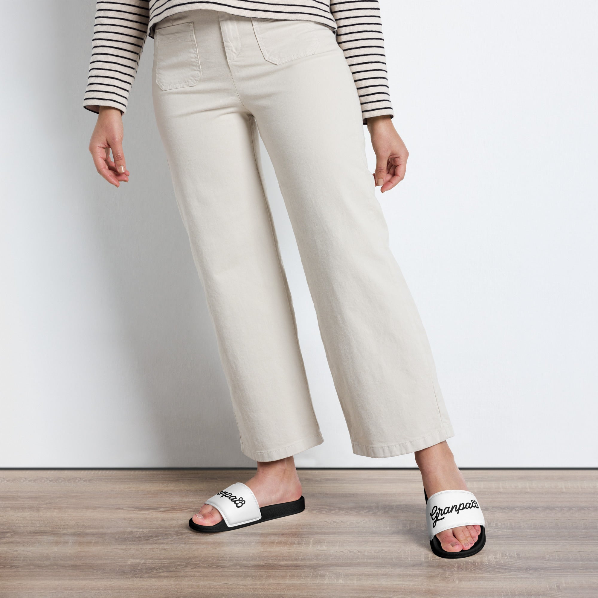 Person wearing white wide-leg pants and white slides with 'granpaw golf' branding on a wooden floor.