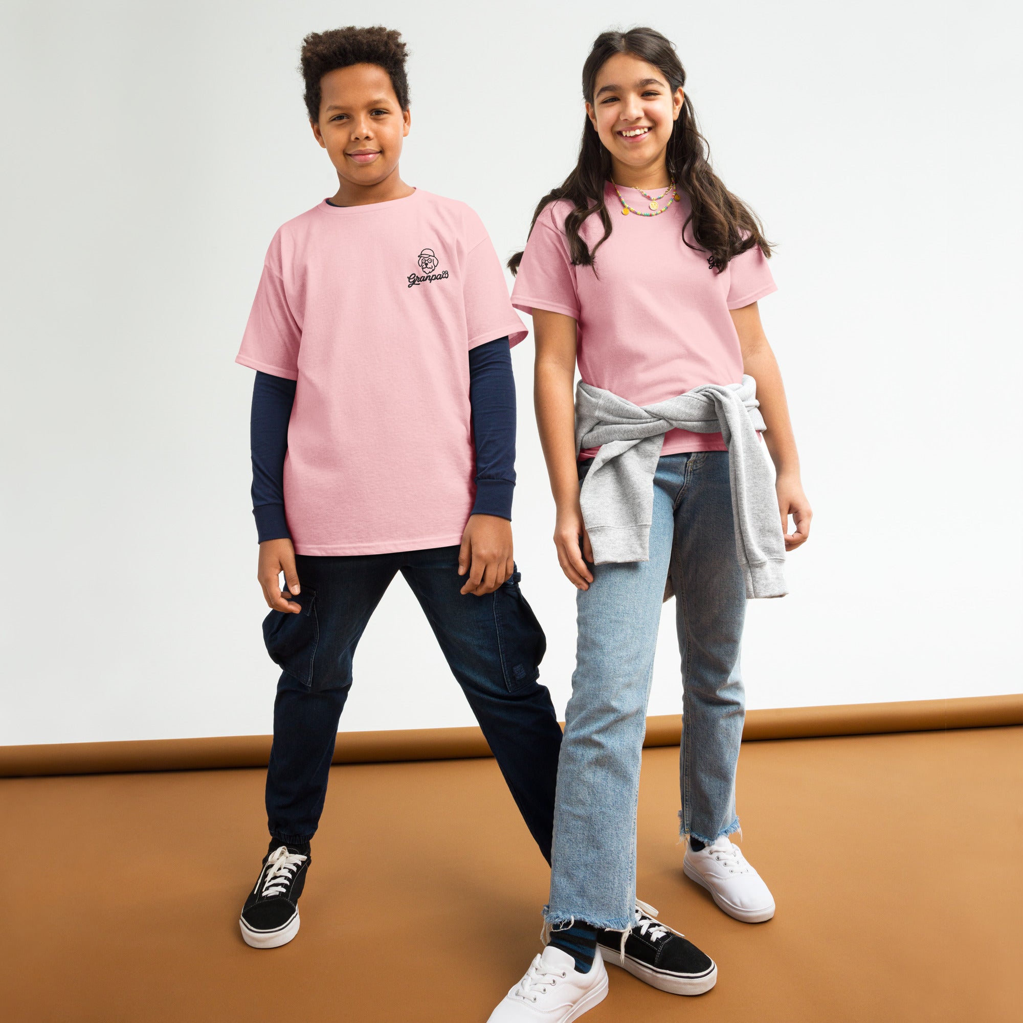 Two children wearing pink shirts standing on a brown surface with a white background