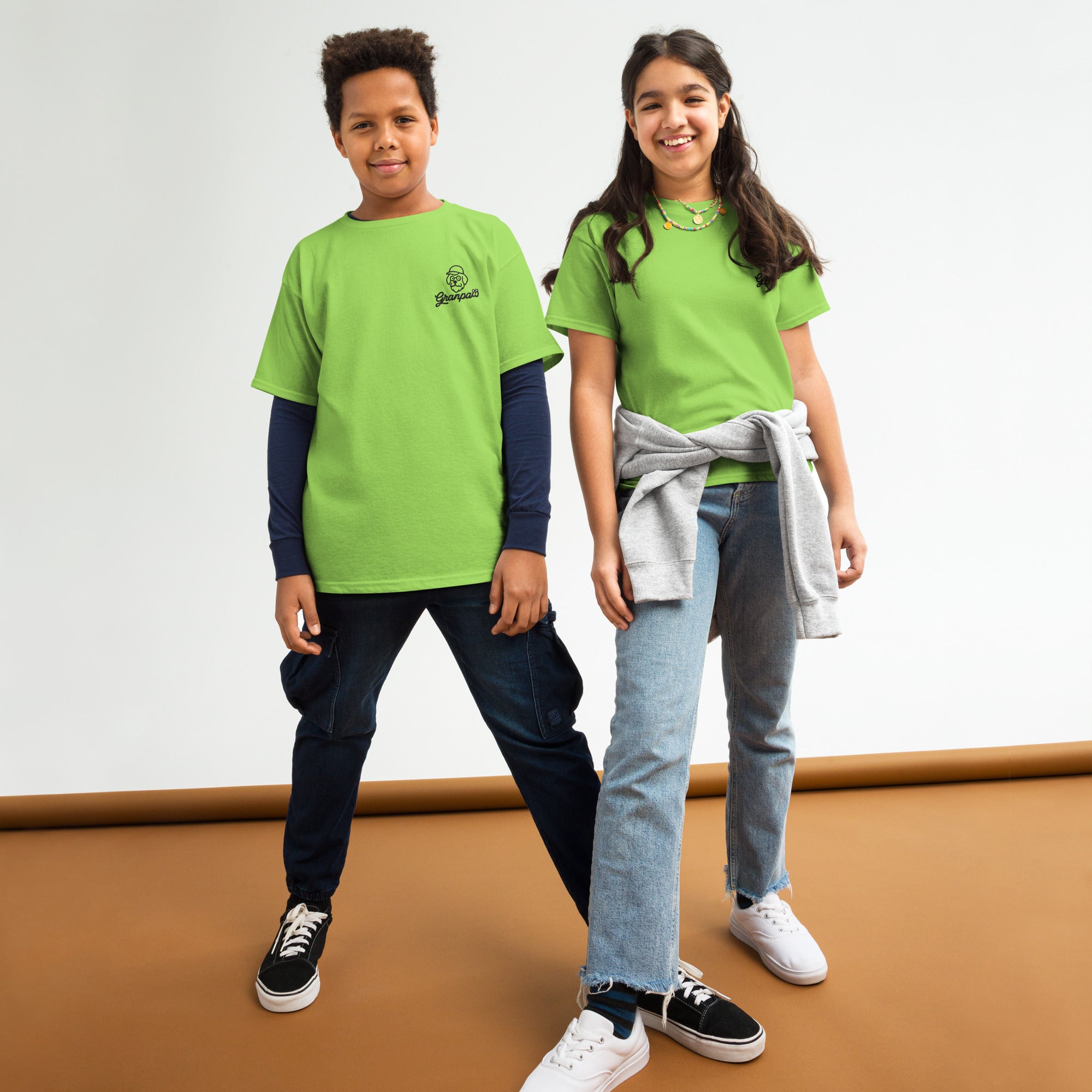 Two children wearing green shirts standing on a brown surface with a white background