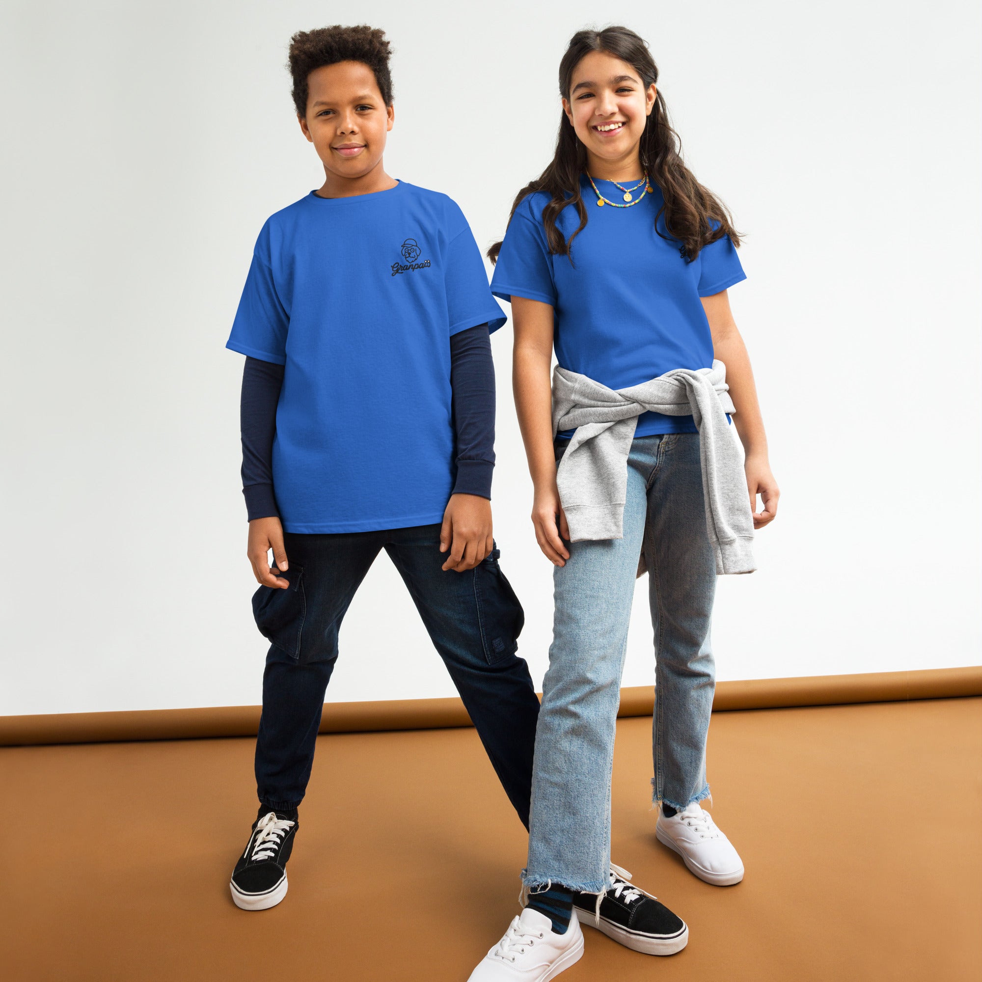 Two children wearing blue shirts standing on a brown surface with a white background