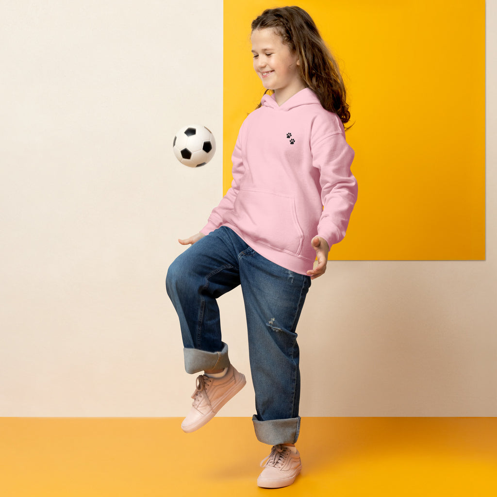 Child in pink hoodie and jeans kicking a soccer ball against a yellow and beige background